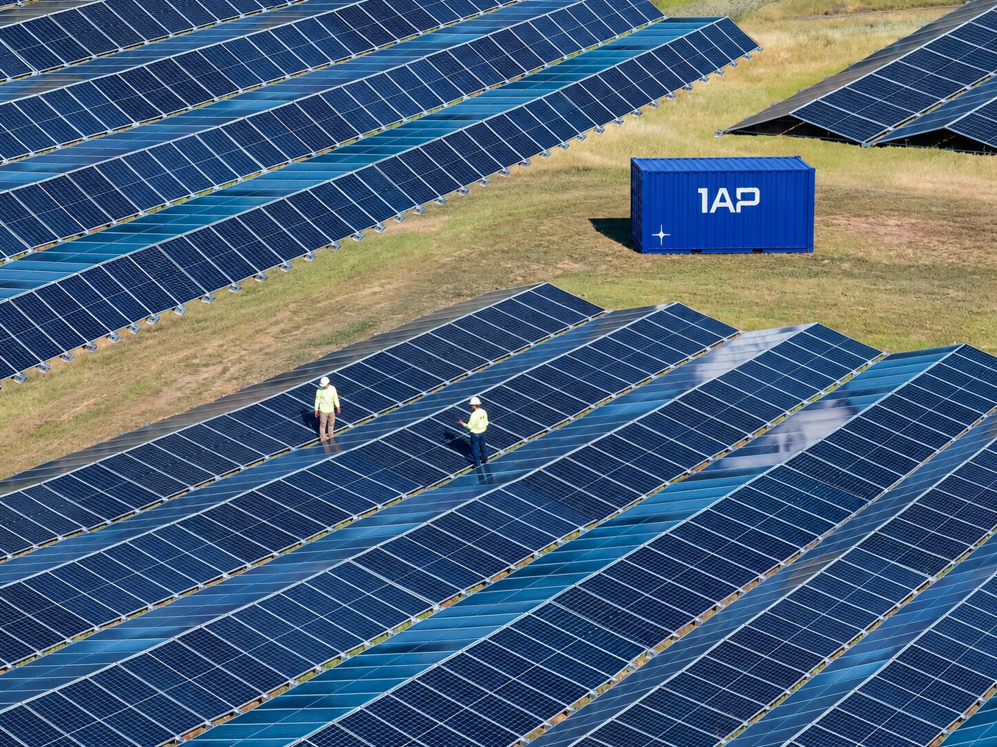 A 1AP power unit beside solar arrays, with two engineers walking the rows